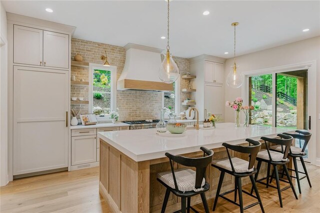 kitchen with a center island with sink, recessed lighting, light countertops, light wood-type flooring, and custom range hood