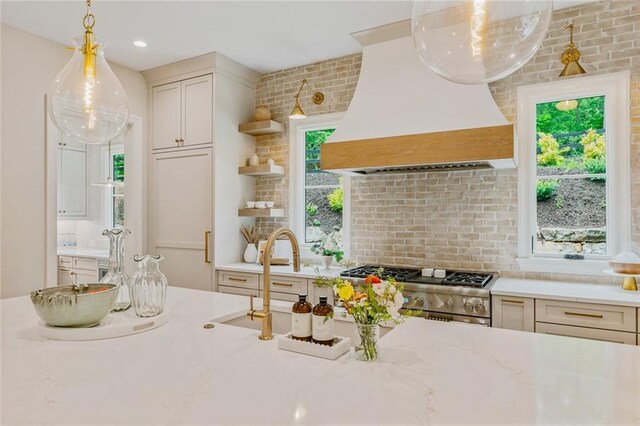 kitchen with pendant lighting, decorative backsplash, premium range hood, a sink, and range
