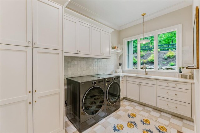 laundry area with crown molding, washing machine and dryer, cabinet space, a sink, and light floors