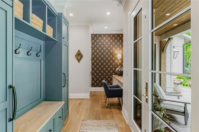 mudroom with crown molding, an accent wall, baseboards, wallpapered walls, and light wood-style flooring