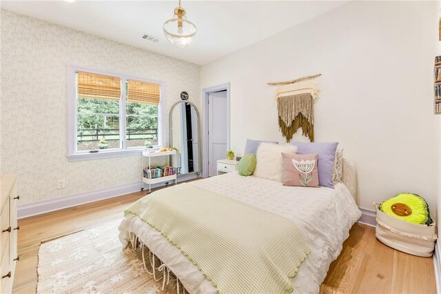 bedroom featuring baseboards, wallpapered walls, wood finished floors, and visible vents