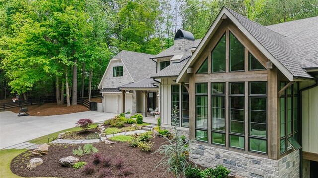 exterior space featuring concrete driveway, a shingled roof, stone siding, and a chimney