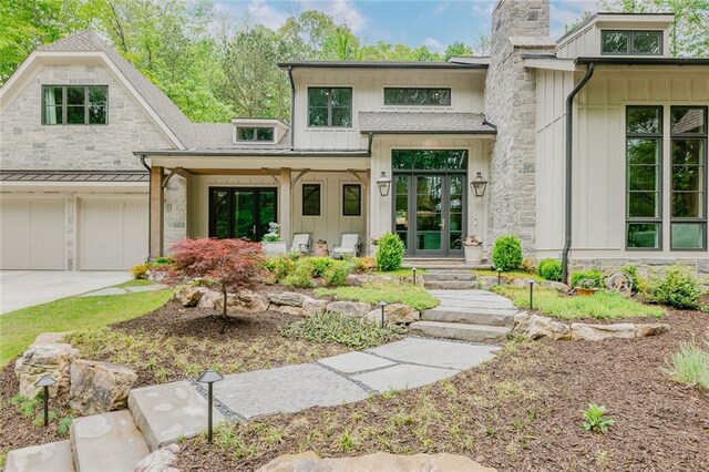doorway to property with board and batten siding, driveway, a chimney, an attached garage, and stone siding