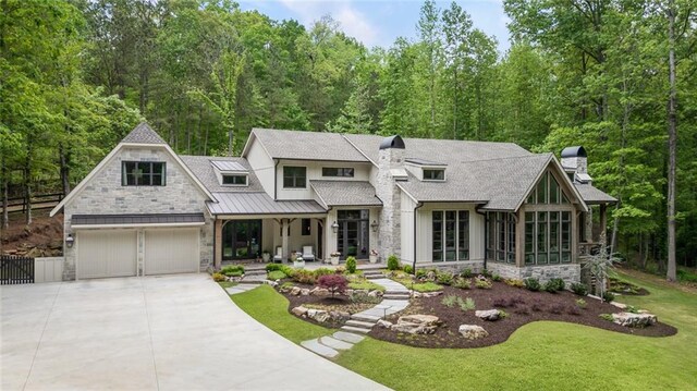 view of front of property featuring a standing seam roof, a chimney, fence, concrete driveway, and stone siding