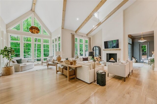 living room with a warm lit fireplace, high vaulted ceiling, light wood-style flooring, and beam ceiling