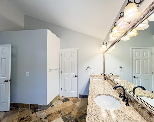 bathroom with a sink, stone tile flooring, baseboards, and vaulted ceiling