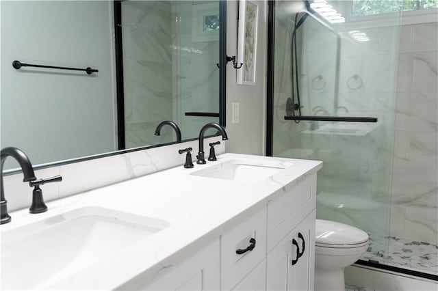 full bath with double vanity, a marble finish shower, a sink, and toilet