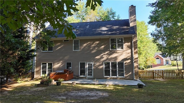 back of property with a hot tub, a lawn, a chimney, fence, and a patio