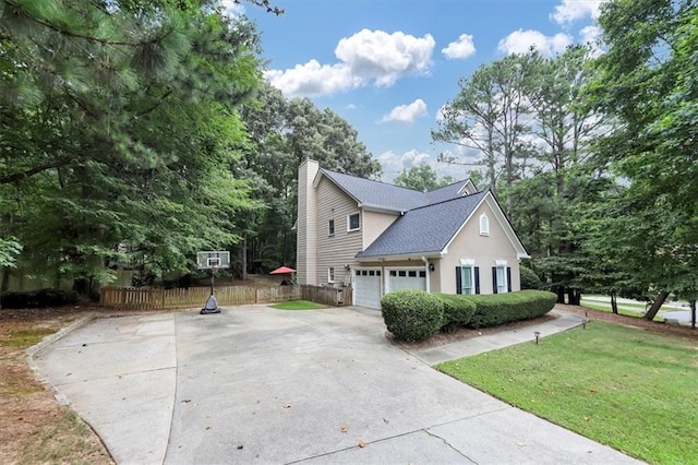 view of side of home featuring concrete driveway, a chimney, an attached garage, fence, and a lawn