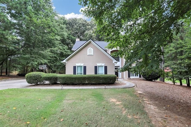 view of front of home featuring a front yard, stucco siding, a chimney, and dirt driveway