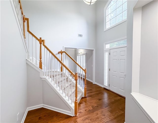 foyer entrance with visible vents, baseboards, a high ceiling, wood finished floors, and stairs