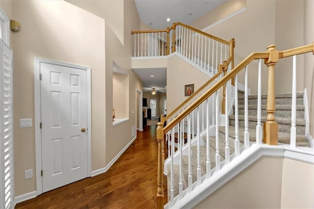staircase with baseboards, a ceiling fan, a towering ceiling, and wood finished floors