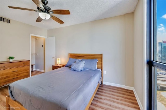 bedroom featuring baseboards, visible vents, a ceiling fan, a textured ceiling, and light wood-type flooring