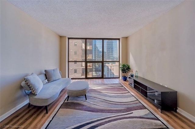living area featuring a textured ceiling, wood finished floors, baseboards, and floor to ceiling windows