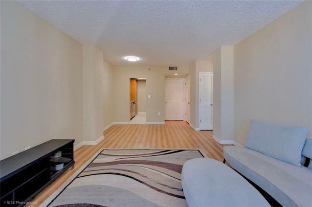 living room with light wood-style floors, visible vents, baseboards, and a textured ceiling