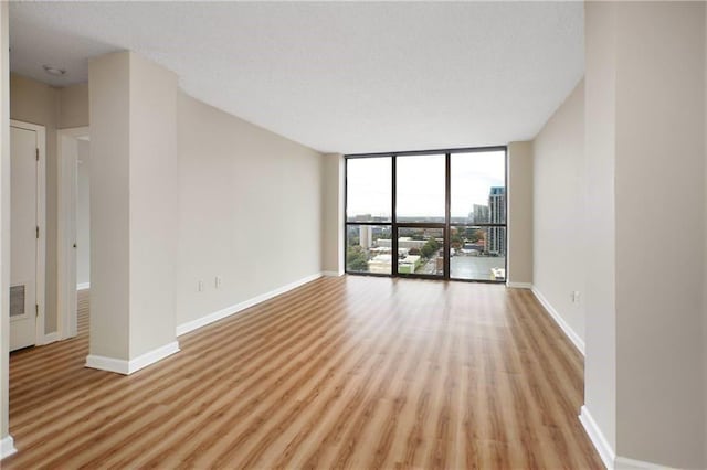 empty room with baseboards, a wall of windows, visible vents, and light wood-style floors