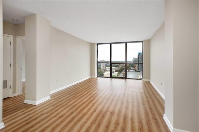 empty room with light wood-style flooring, a wall of windows, baseboards, and visible vents
