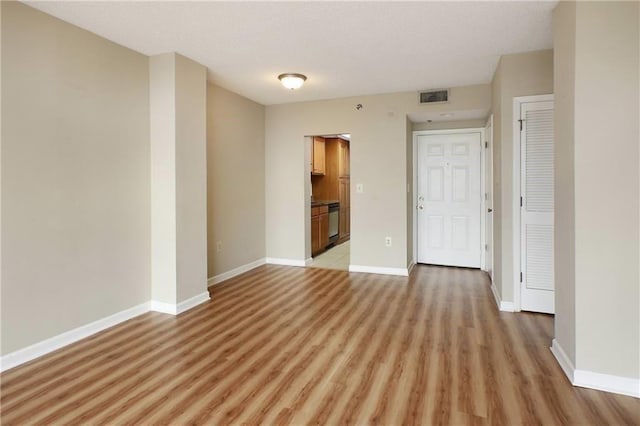 empty room with light wood finished floors, visible vents, and baseboards