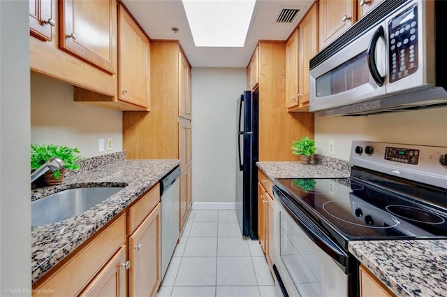 kitchen with a skylight, light tile patterned floors, appliances with stainless steel finishes, light stone counters, and a sink