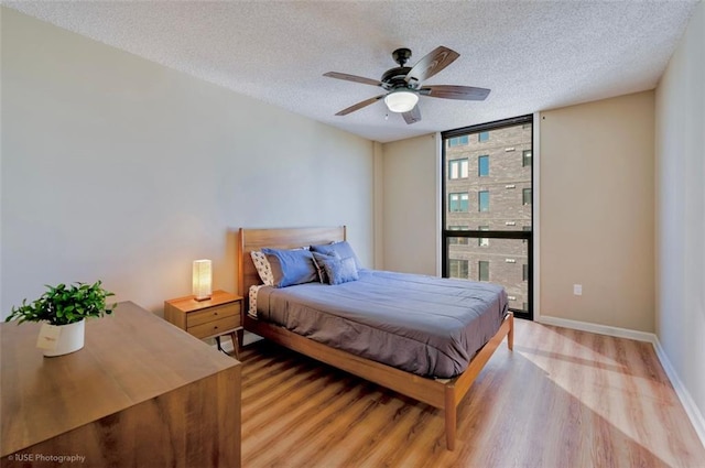 bedroom with a textured ceiling, light wood finished floors, a wall of windows, and baseboards