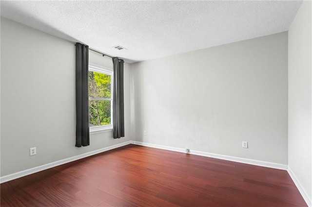 unfurnished room with baseboards, a textured ceiling, wood finished floors, and visible vents
