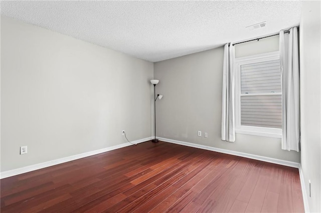 unfurnished room featuring a textured ceiling, baseboards, visible vents, and dark wood-style floors