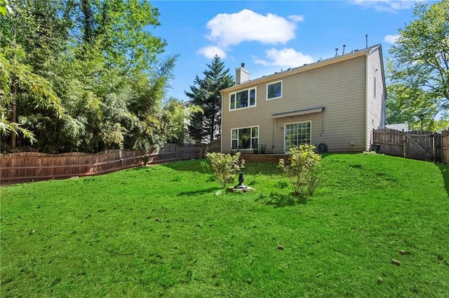 rear view of house featuring a fenced backyard, a chimney, and a lawn