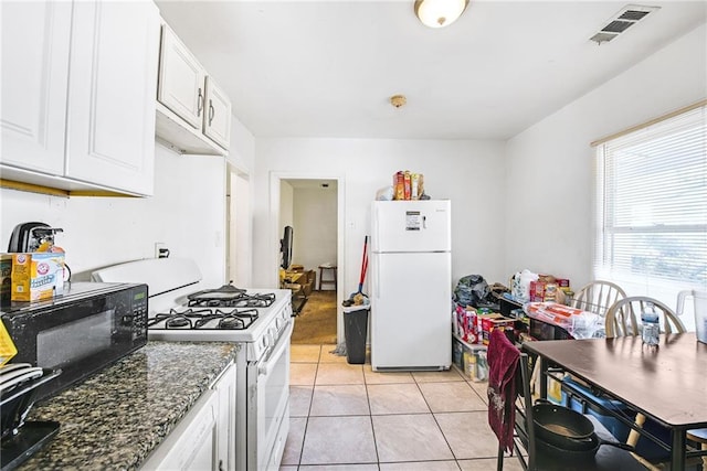 kitchen with light tile patterned floors, white appliances, dark stone counters, and white cabinets