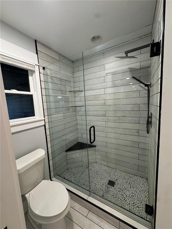 bathroom featuring toilet, an enclosed shower, and wood-type flooring