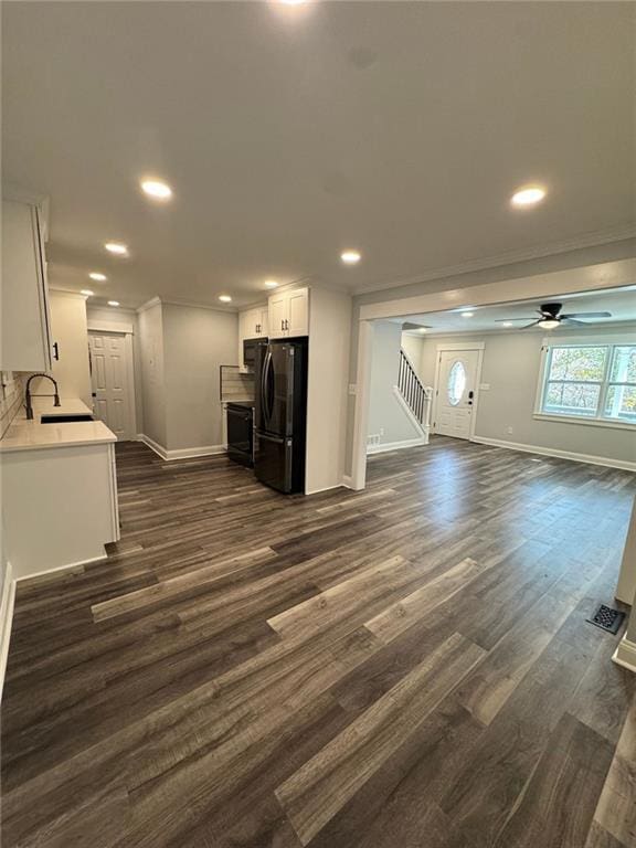 unfurnished living room featuring ceiling fan, sink, dark wood-type flooring, and crown molding