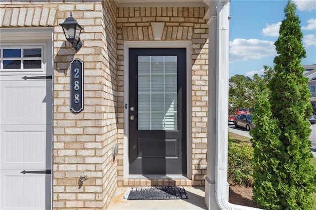 doorway to property with a garage and brick siding