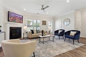 living area with ceiling fan, recessed lighting, wood finished floors, ornamental molding, and a glass covered fireplace