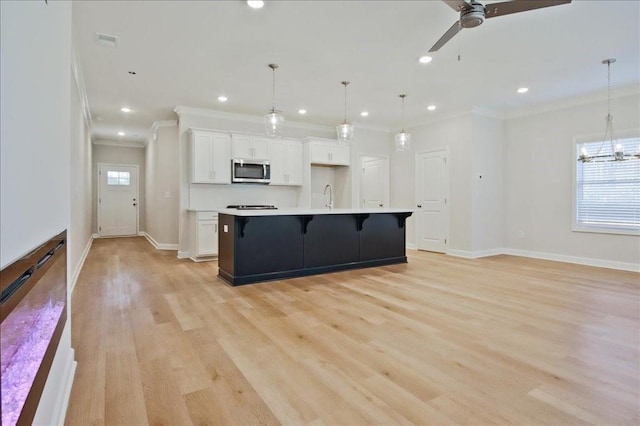 kitchen featuring a large island with sink, white cabinetry, decorative light fixtures, and light wood-type flooring