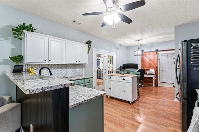 kitchen with ceiling fan, kitchen peninsula, white cabinetry, a barn door, and black refrigerator