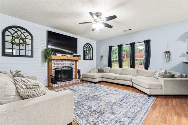 living room featuring wood-type flooring, a textured ceiling, wood walls, a brick fireplace, and ceiling fan