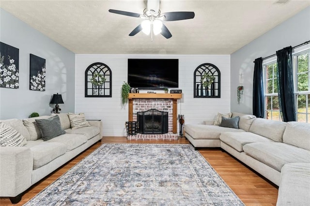 living room featuring a brick fireplace, ceiling fan, hardwood / wood-style flooring, and a textured ceiling