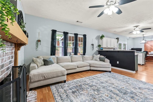 living room featuring light hardwood / wood-style floors, ceiling fan, a fireplace, and a textured ceiling