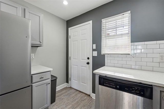 kitchen featuring tasteful backsplash, gray cabinetry, light wood-type flooring, and appliances with stainless steel finishes