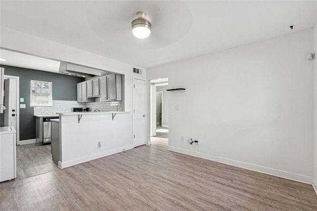 kitchen with ceiling fan, washer / clothes dryer, wood-type flooring, decorative backsplash, and a breakfast bar