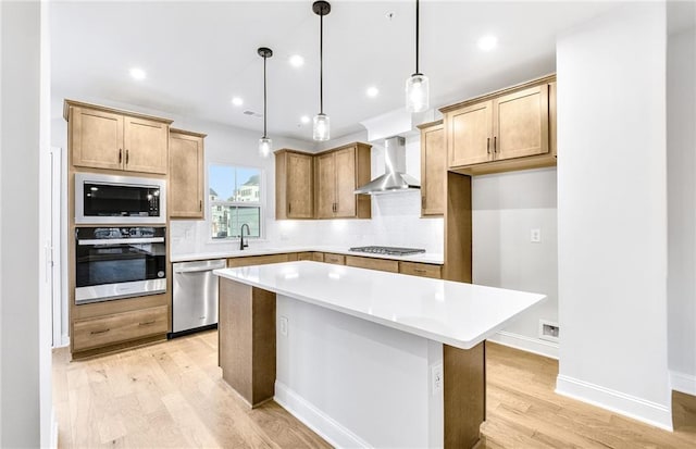 kitchen with a center island, wall chimney range hood, light wood-type flooring, pendant lighting, and stainless steel appliances