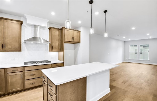 kitchen featuring pendant lighting, wall chimney exhaust hood, decorative backsplash, light hardwood / wood-style floors, and stainless steel gas stovetop