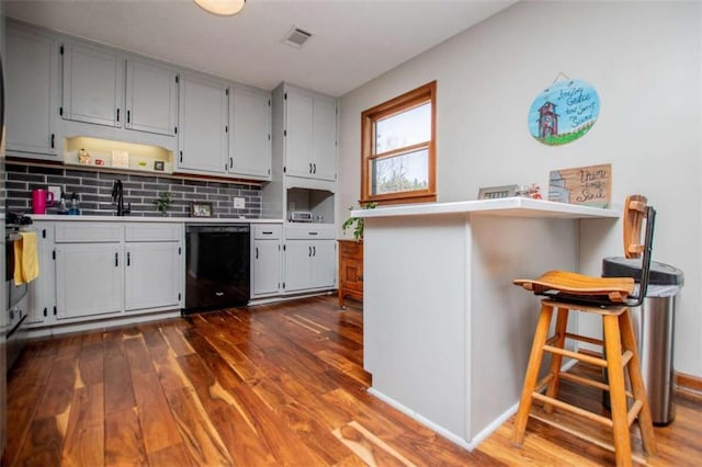 kitchen with a sink, dark wood-style floors, light countertops, dishwasher, and tasteful backsplash