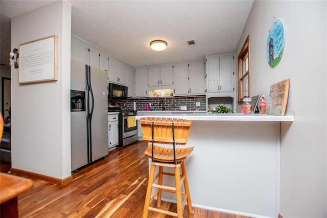 kitchen featuring a peninsula, dark wood-type flooring, visible vents, appliances with stainless steel finishes, and backsplash