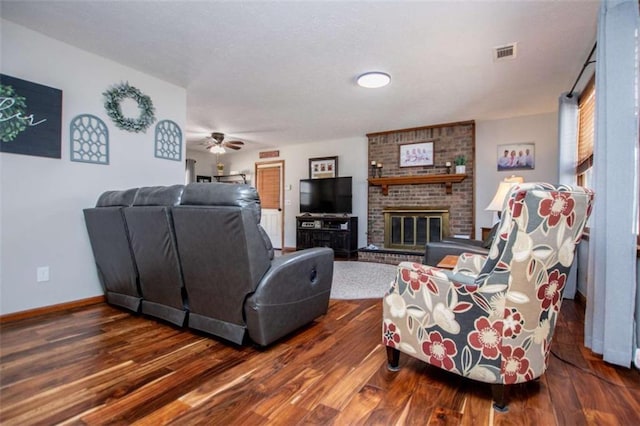 living area with a fireplace, visible vents, ceiling fan, wood finished floors, and baseboards