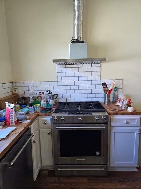 kitchen with white cabinets, stainless steel appliances, range hood, and wood counters