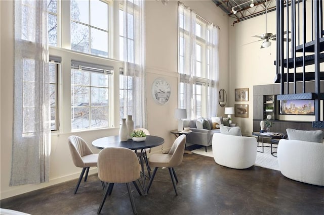 dining room with ceiling fan, a towering ceiling, baseboards, and finished concrete flooring