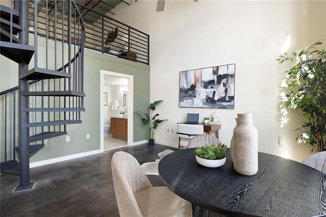 dining space featuring baseboards, a ceiling fan, stairway, a high ceiling, and concrete floors