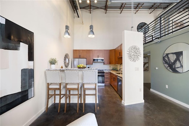 kitchen featuring stainless steel appliances, light countertops, brown cabinetry, concrete flooring, and baseboards