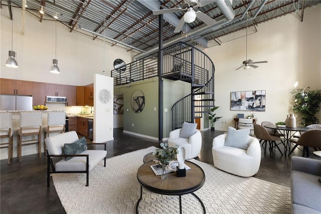 living area with baseboards, a ceiling fan, stairway, finished concrete floors, and a high ceiling