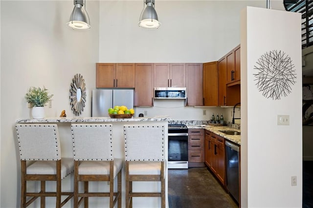 kitchen featuring a towering ceiling, light stone counters, appliances with stainless steel finishes, a kitchen breakfast bar, and a sink